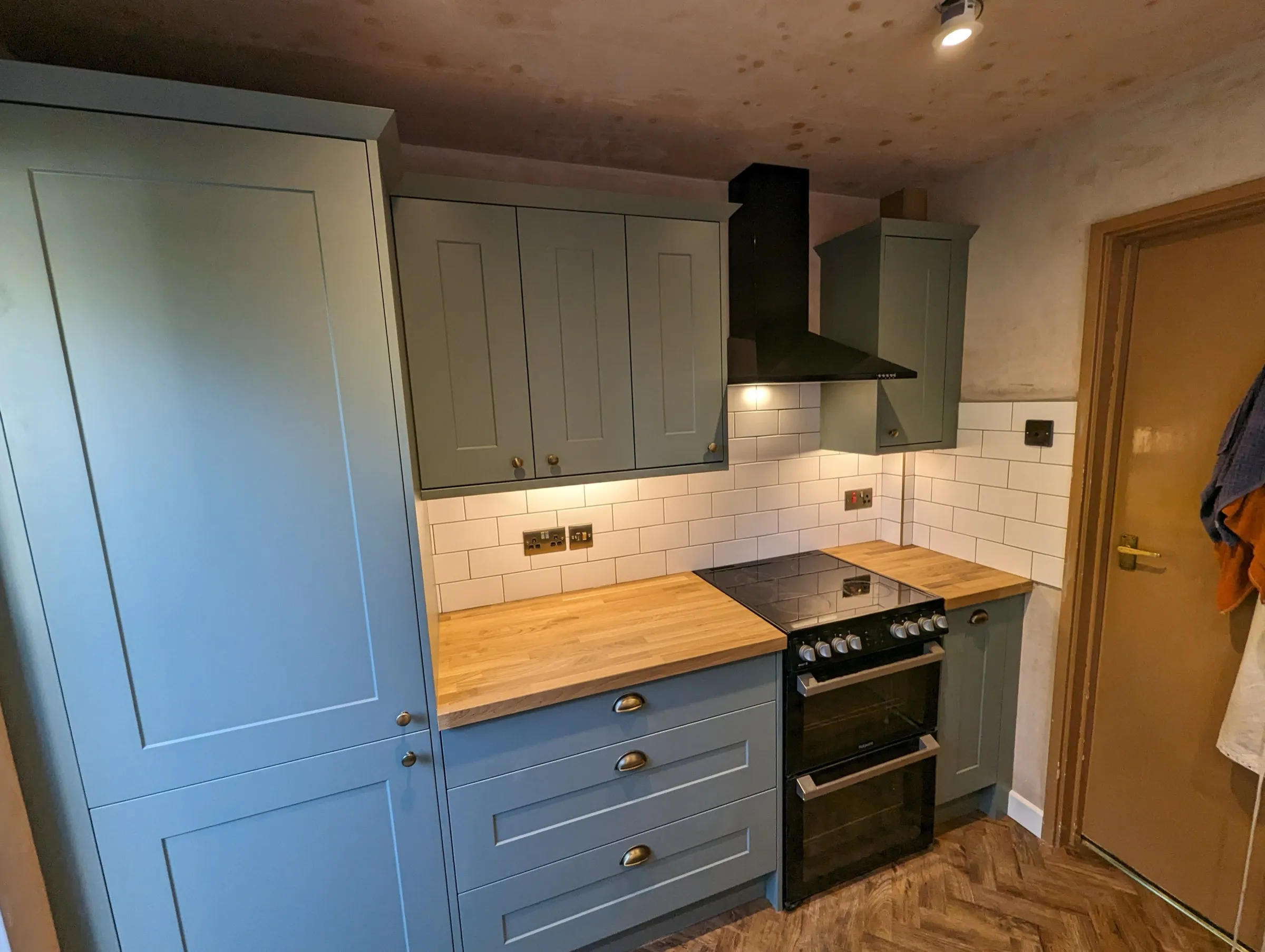 Black freestanding cooker flanked by sage green Shaker units and oak worktops