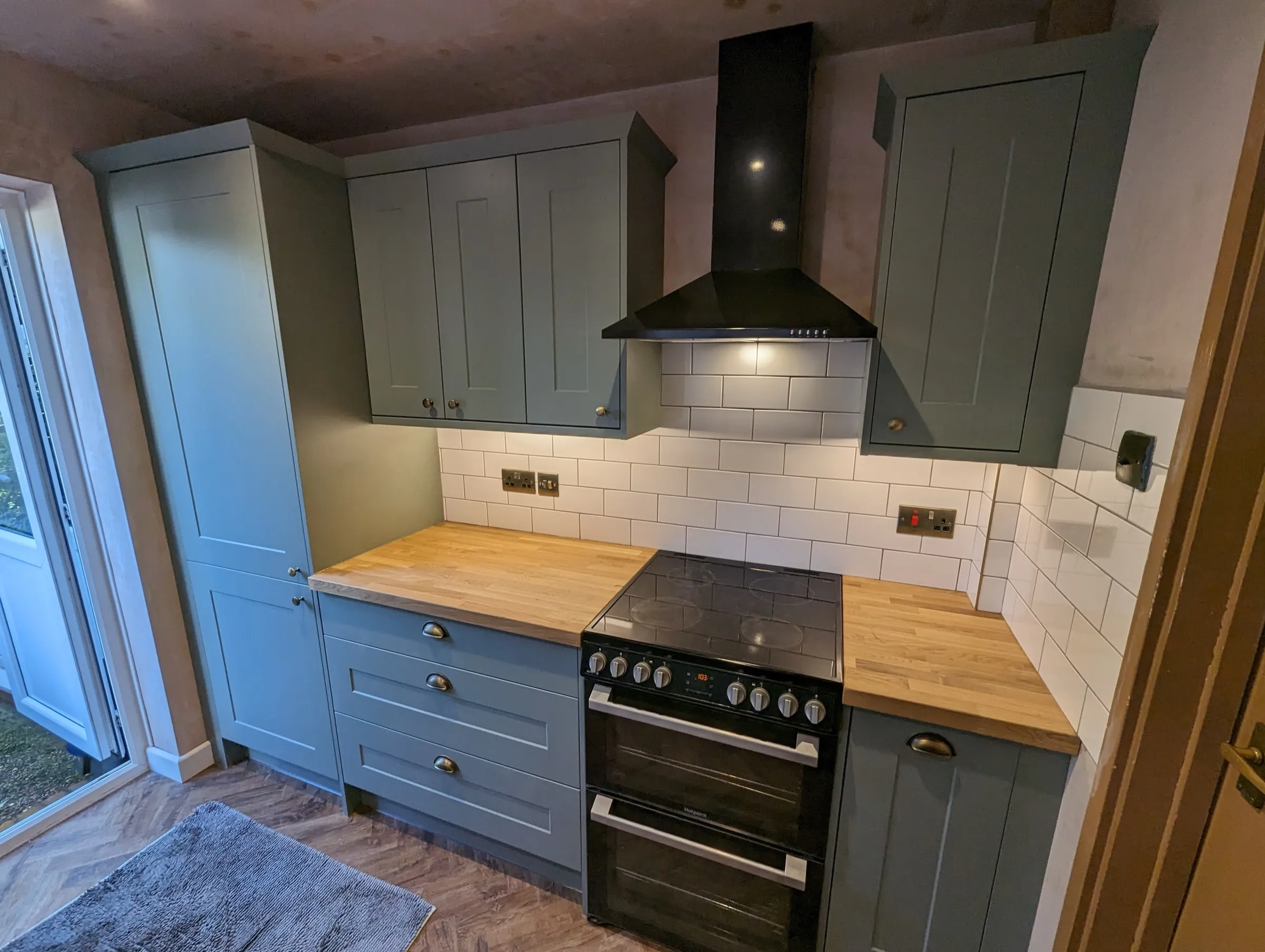 Sage green galley with tall larder units, under-cabinet lighting and parquet-style flooring