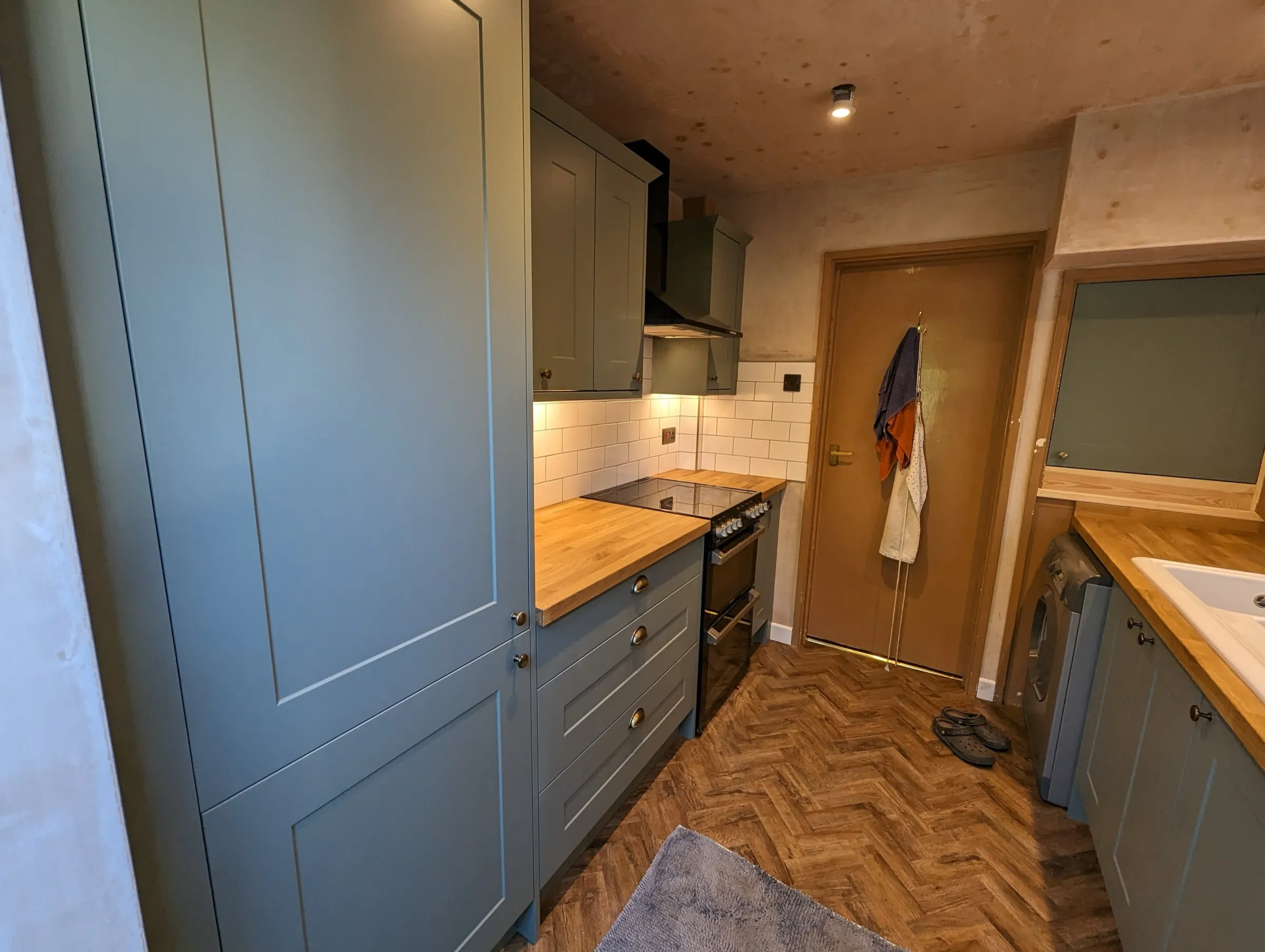 Compact sage green galley kitchen with solid oak worktops and white metro splashback