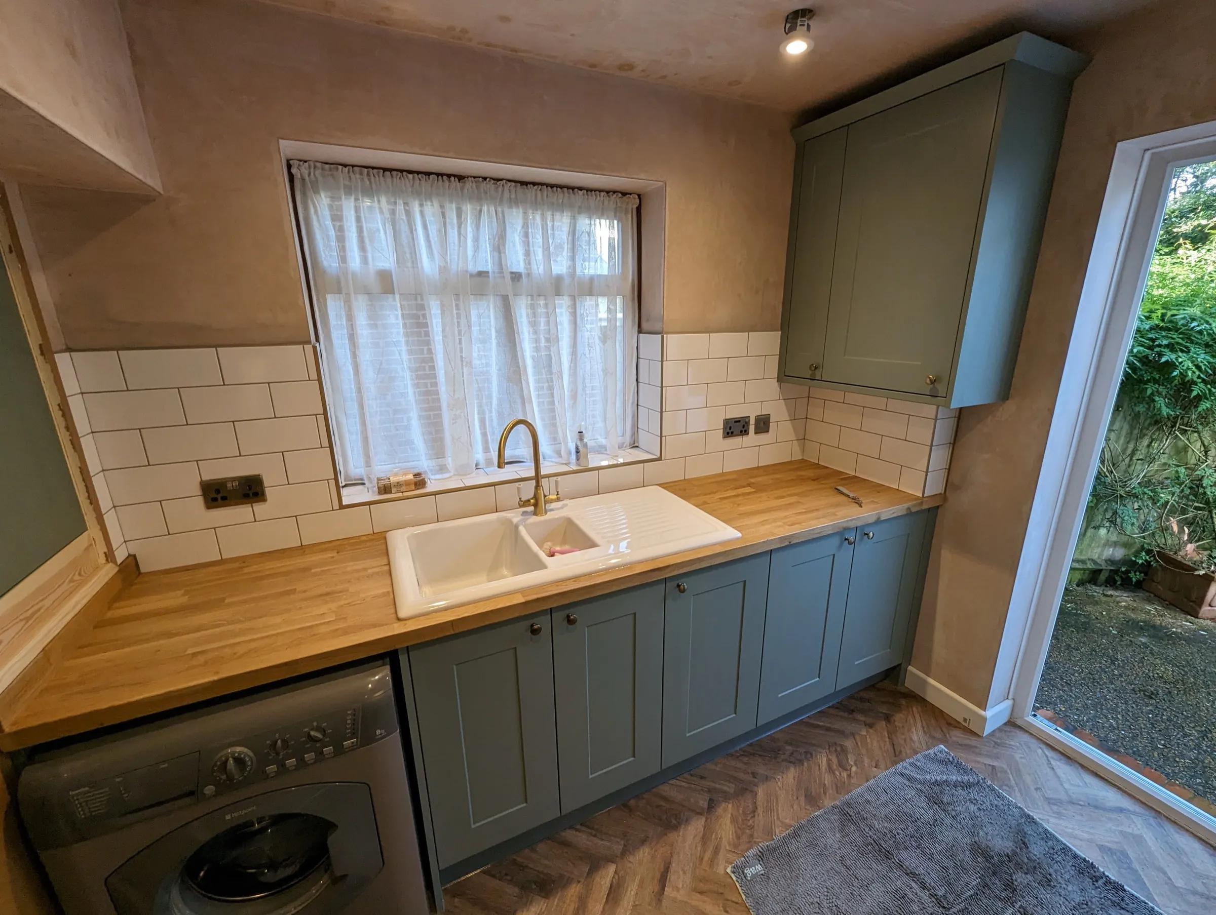 Green Shaker sink wall with oak worktops, metro tiles and door to the garden