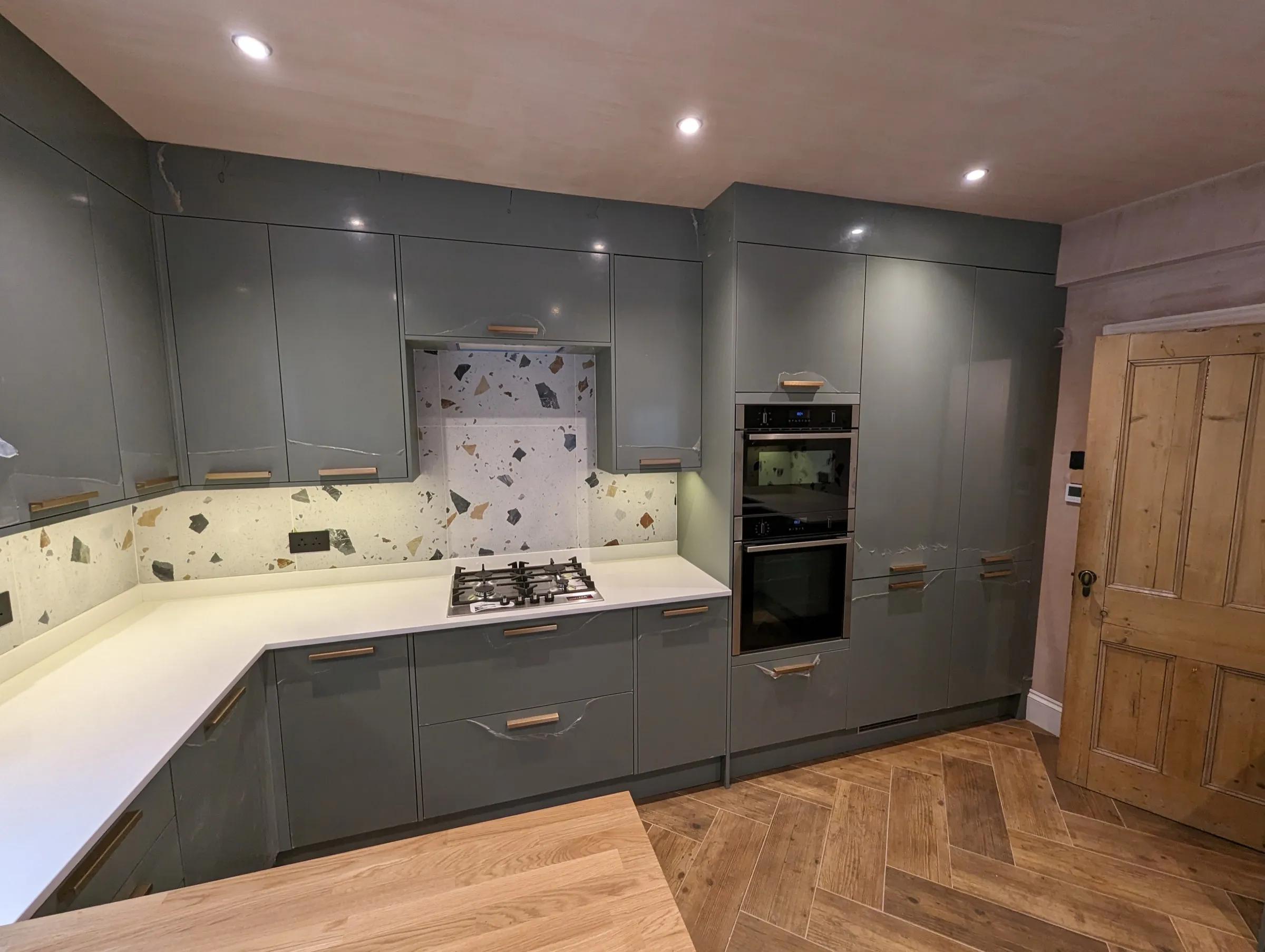 Grey-green kitchen with terrazzo splashback, white quartz worktops and built-in double oven
