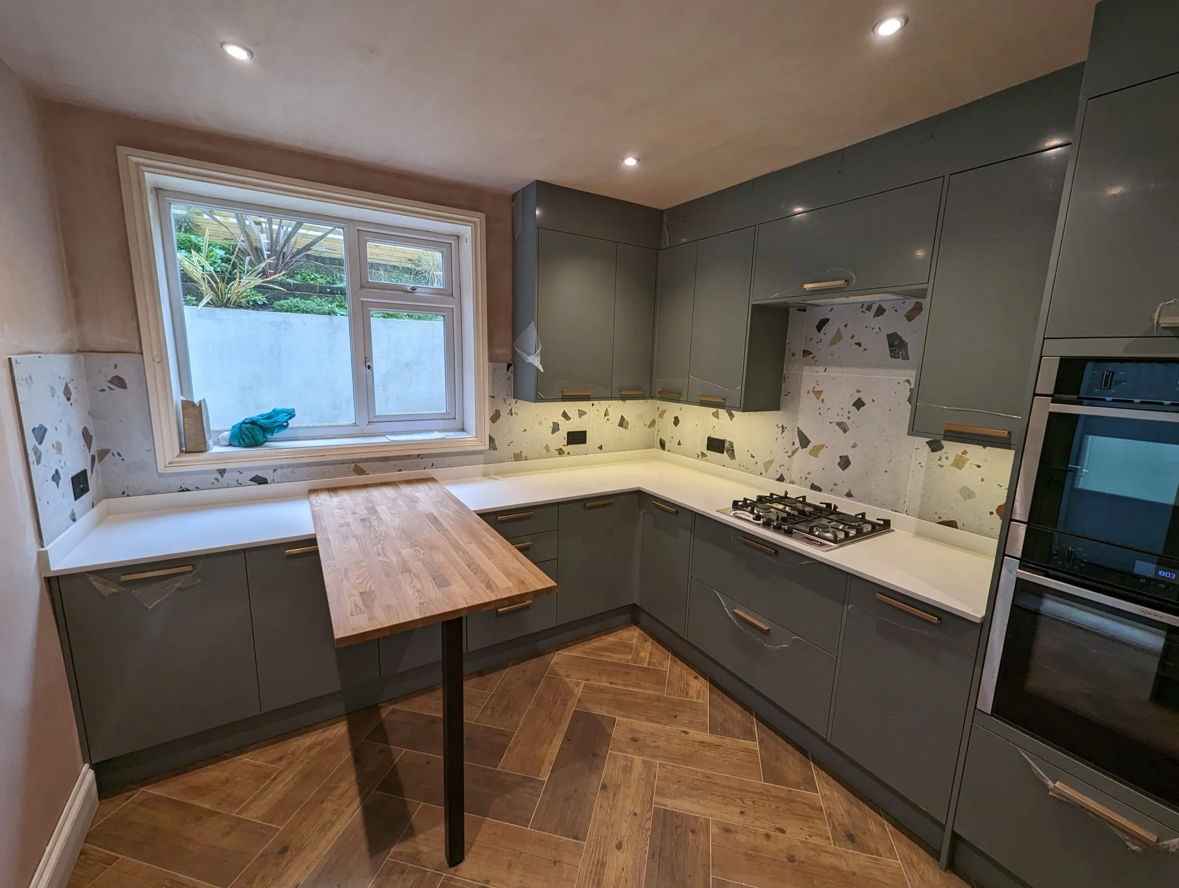L-shaped terrazzo-splashback kitchen with gas hob and oak breakfast peninsula