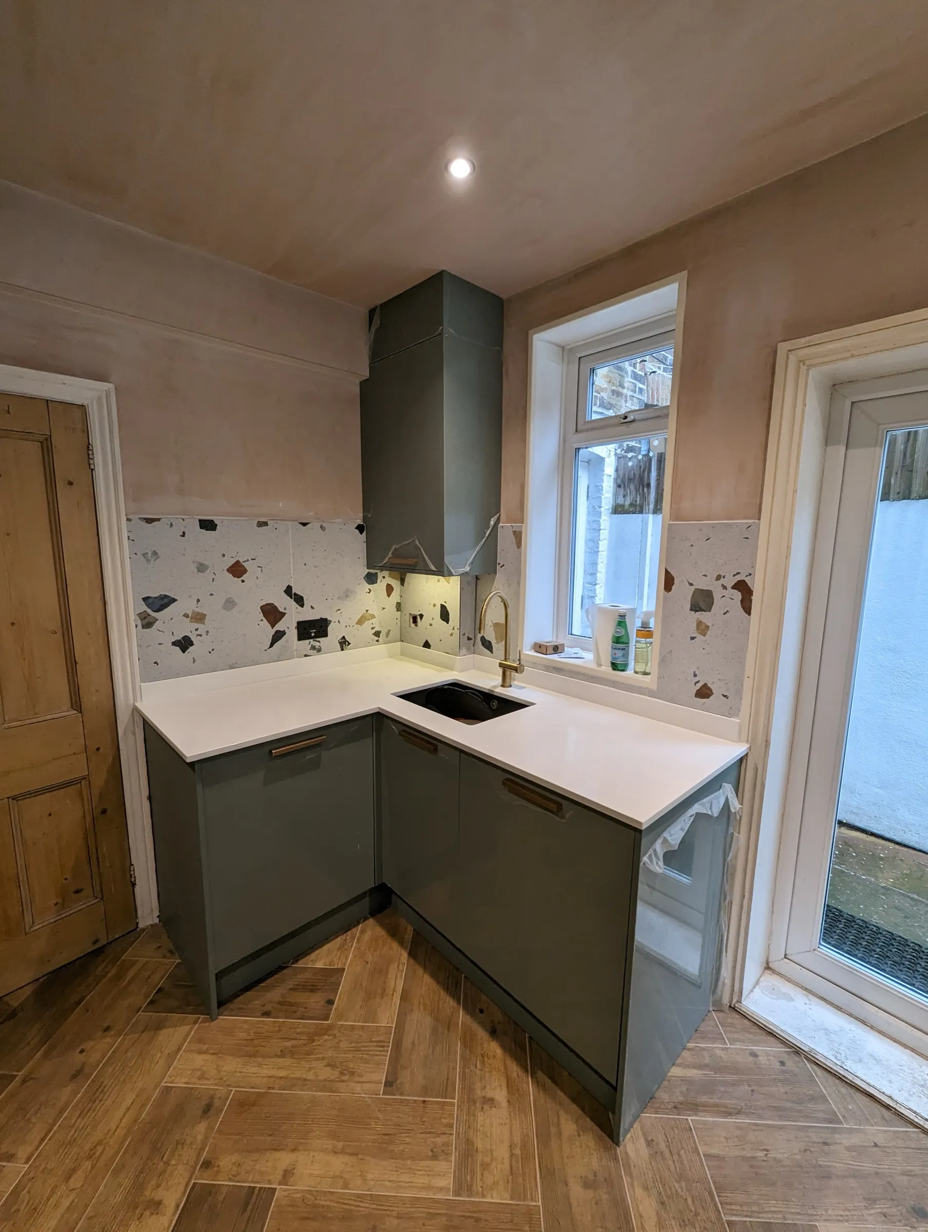 Corner sink with brass tap and terrazzo splashback beside the glazed garden door