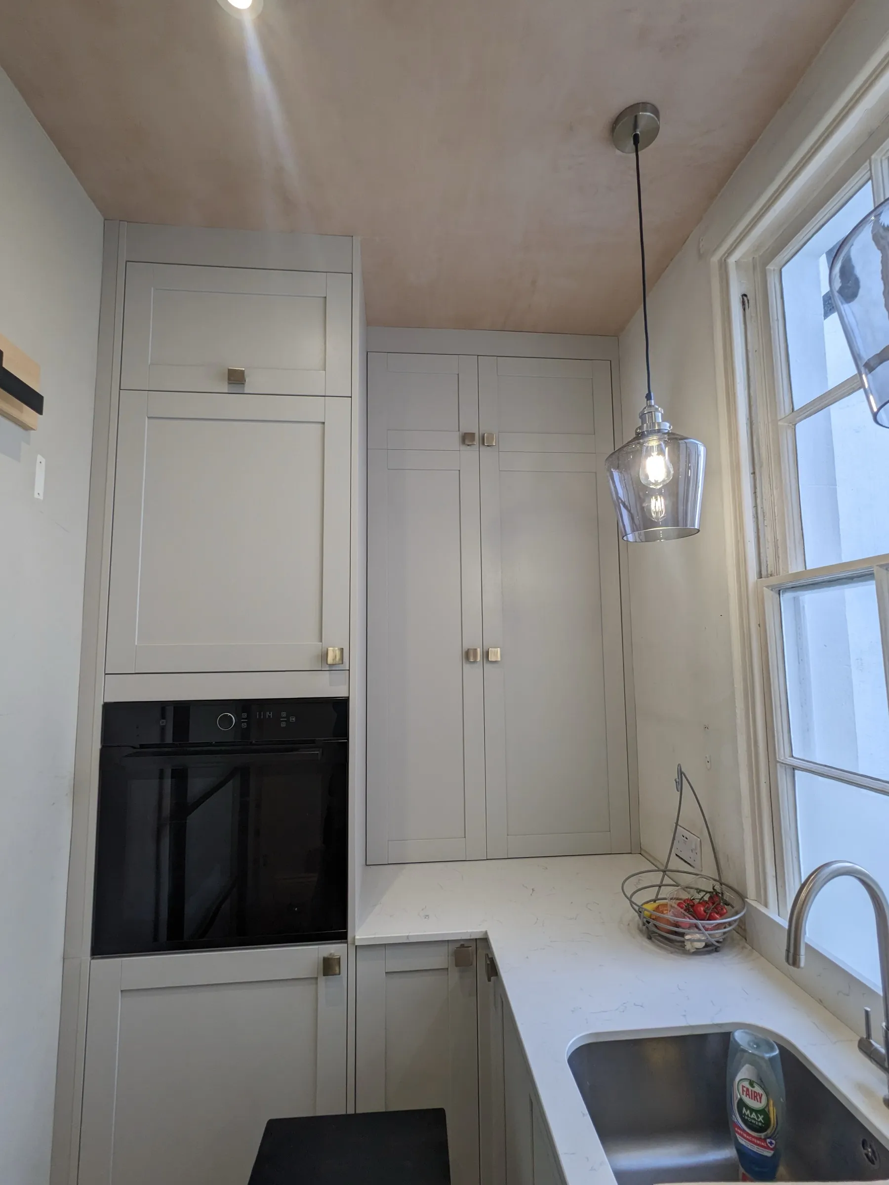 Tall pale grey cabinetry with built-in oven and smoked-glass pendant light