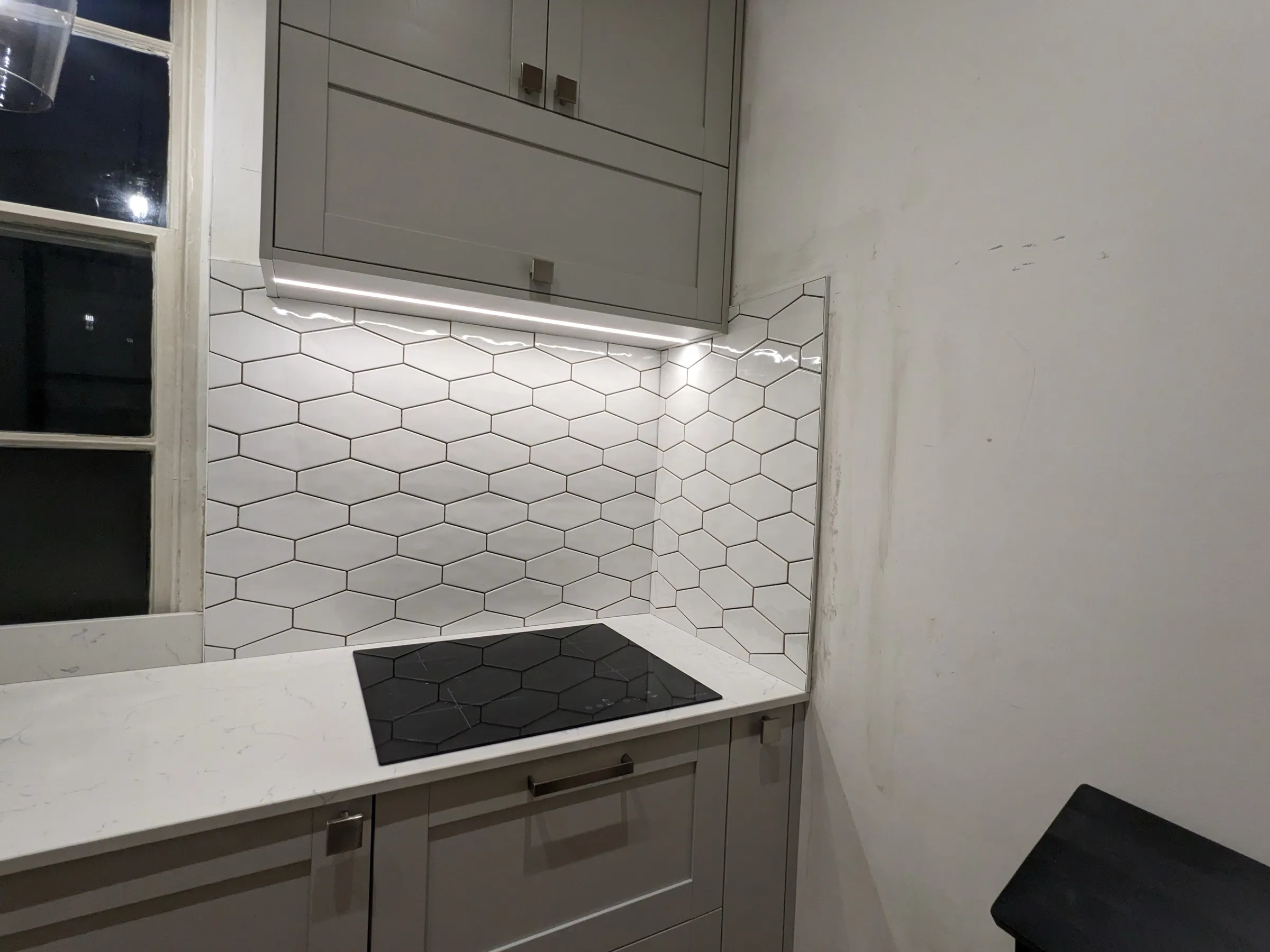 Hexagon-tiled splashback and matching hexagon-patterned induction hob under LED lighting