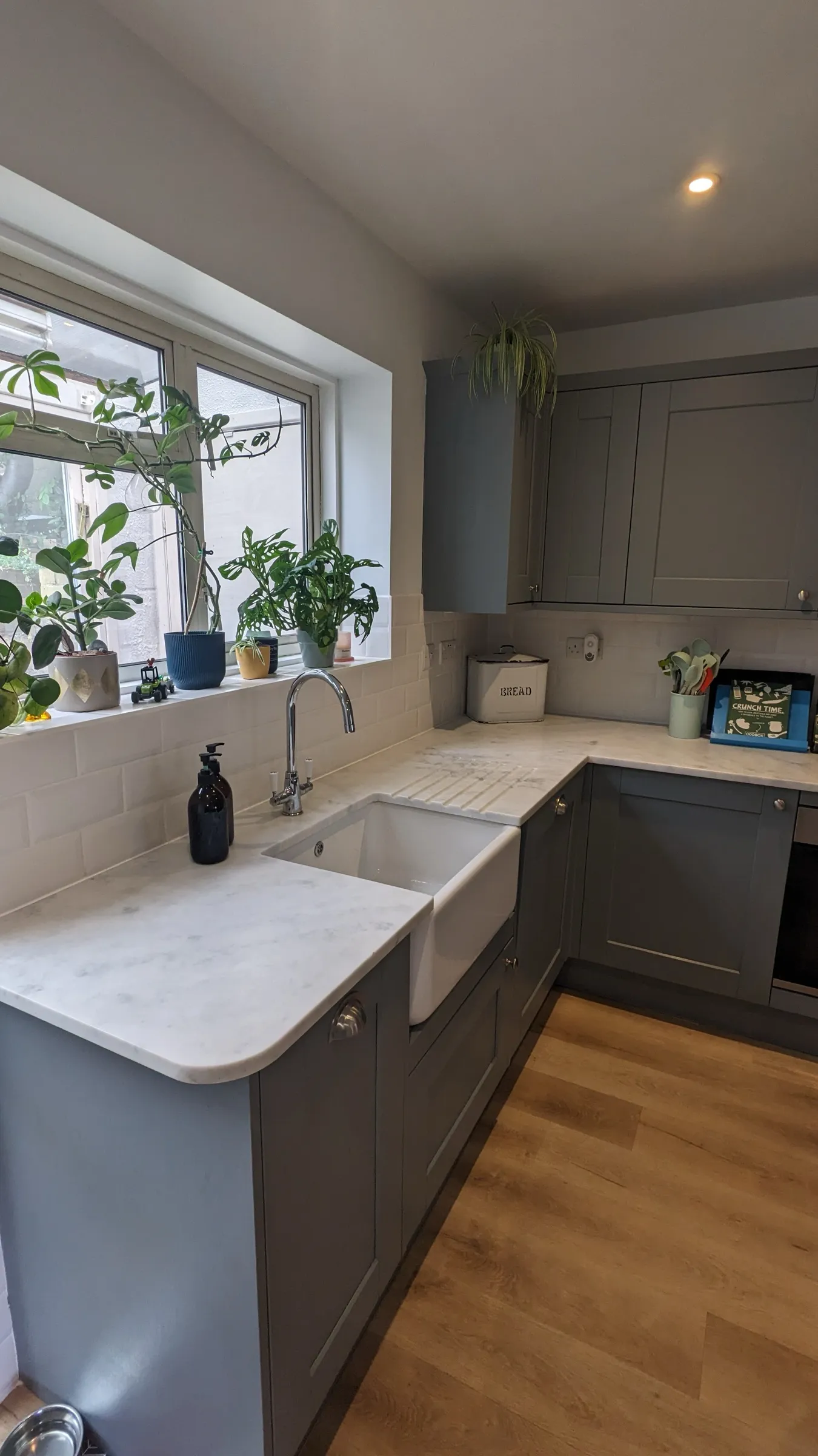 Belfast sink and marble-effect worktop below a windowsill of houseplants