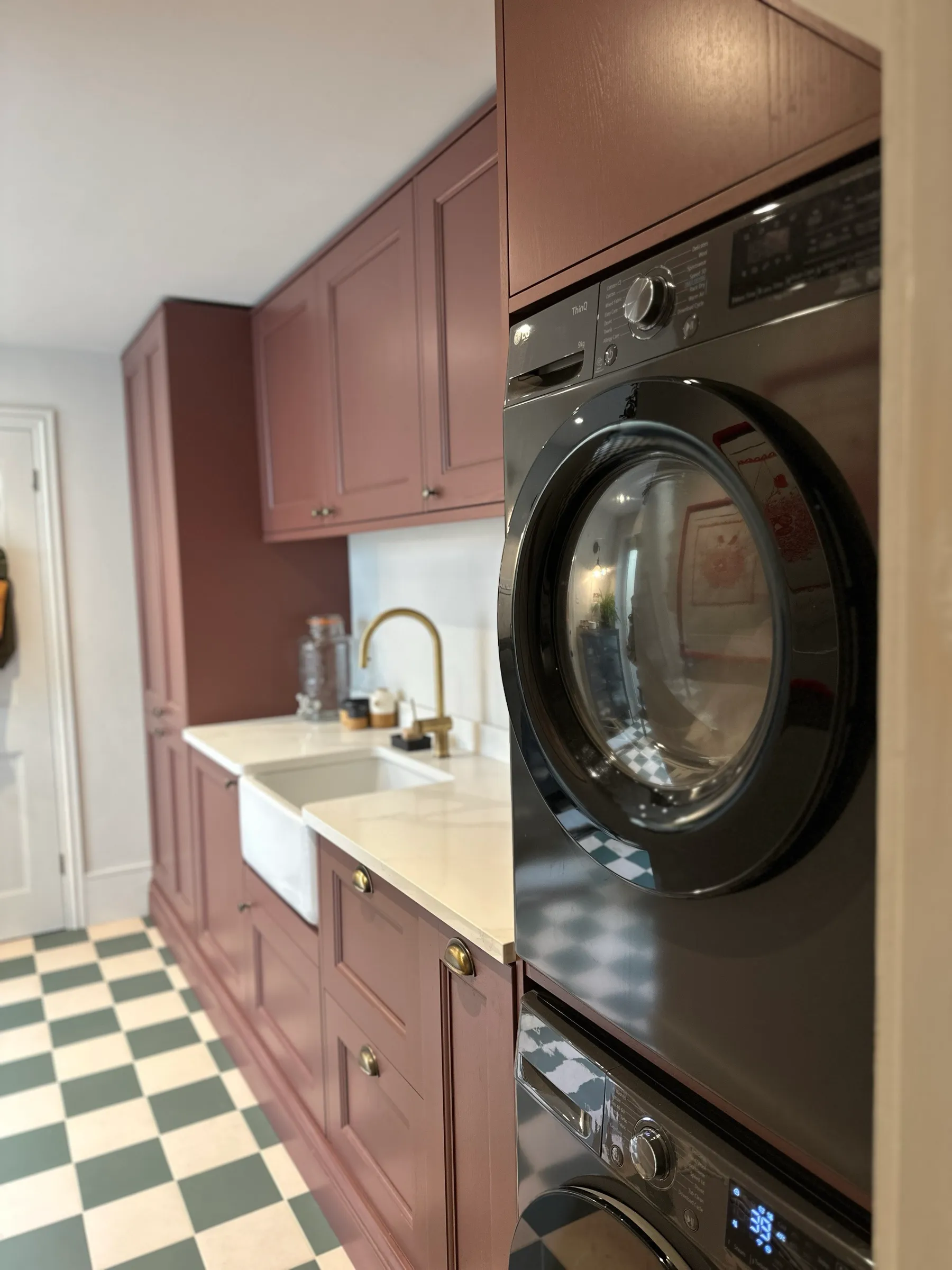 View from the doorway past the stacked washer and dryer to the Belfast sink and maroon Shaker units