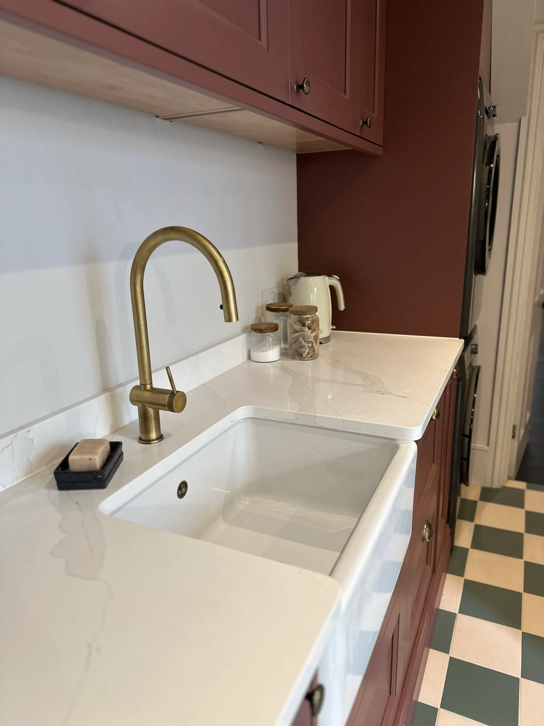 Aged brass swan-neck tap over a white ceramic Belfast sink set in veined quartz worktop