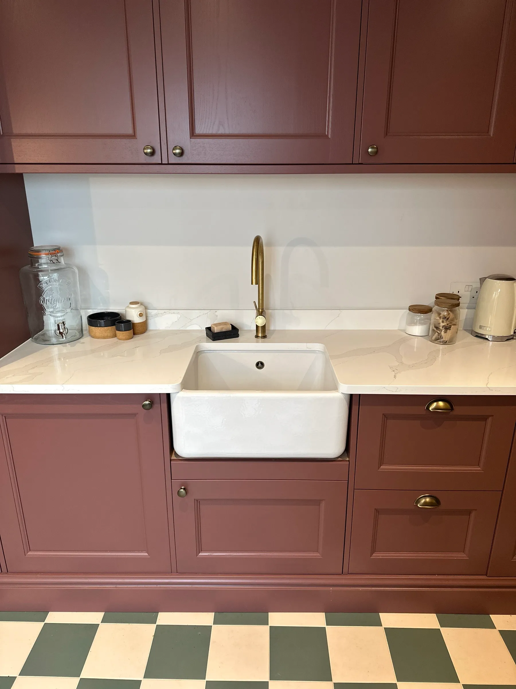 Straight-on view of the Belfast sink flanked by maroon drawers with brass cup handles beneath matching wall cabinets