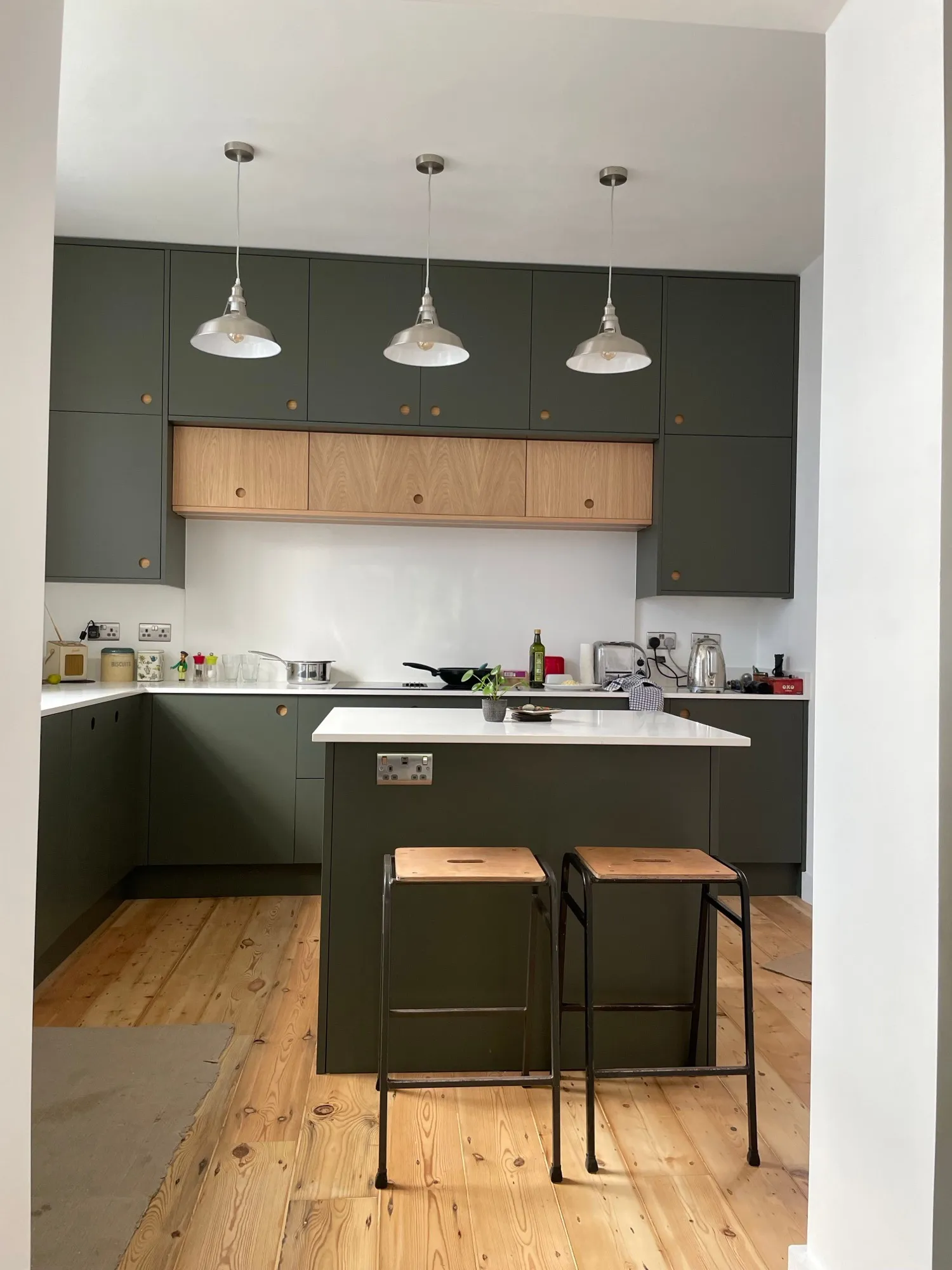 Olive green kitchen with white worktop, oak drawer bank and breakfast bar with industrial stools