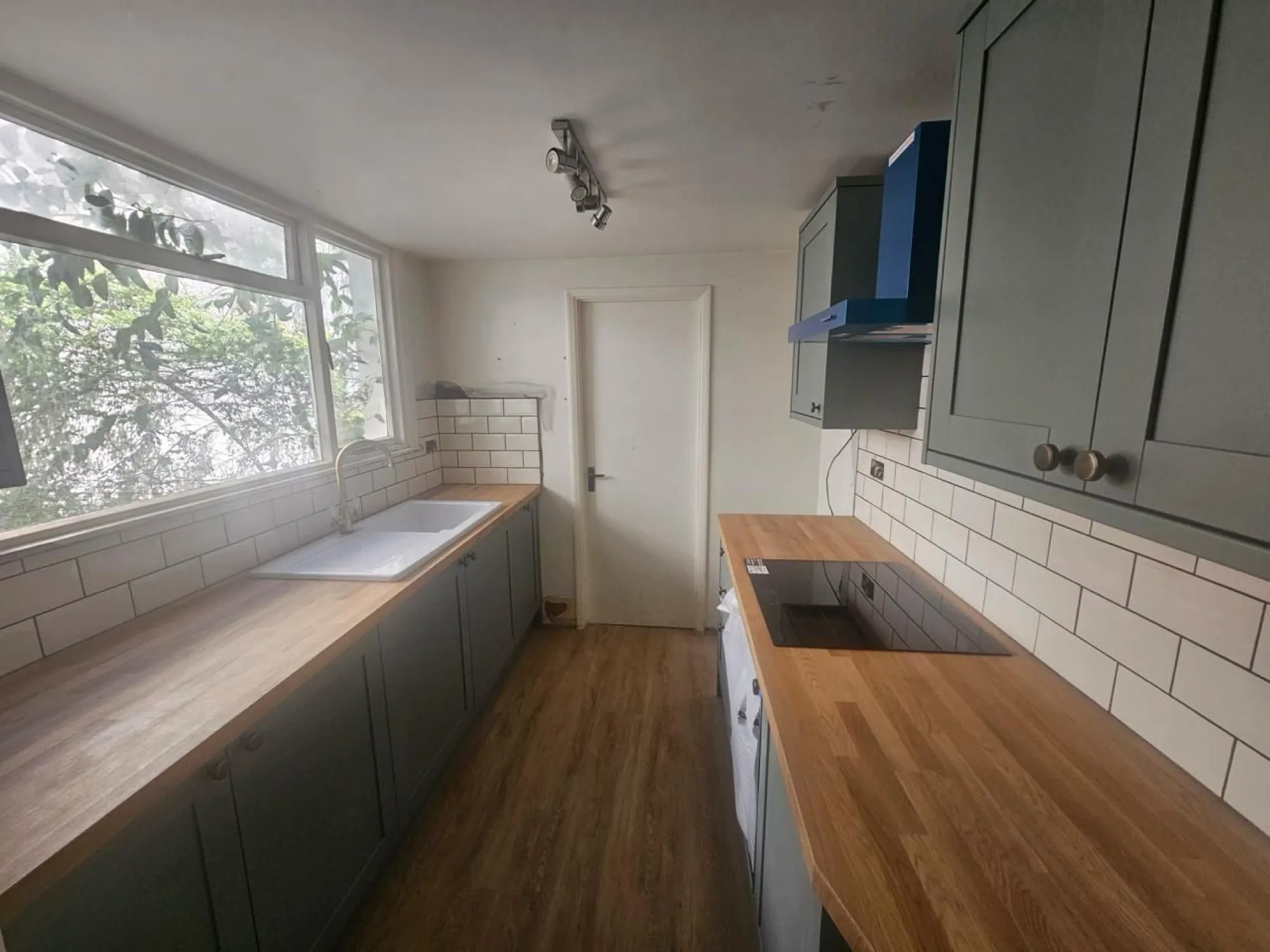 Sage green Shaker kitchen with oak worktops, white metro tiles and navy cooker hood