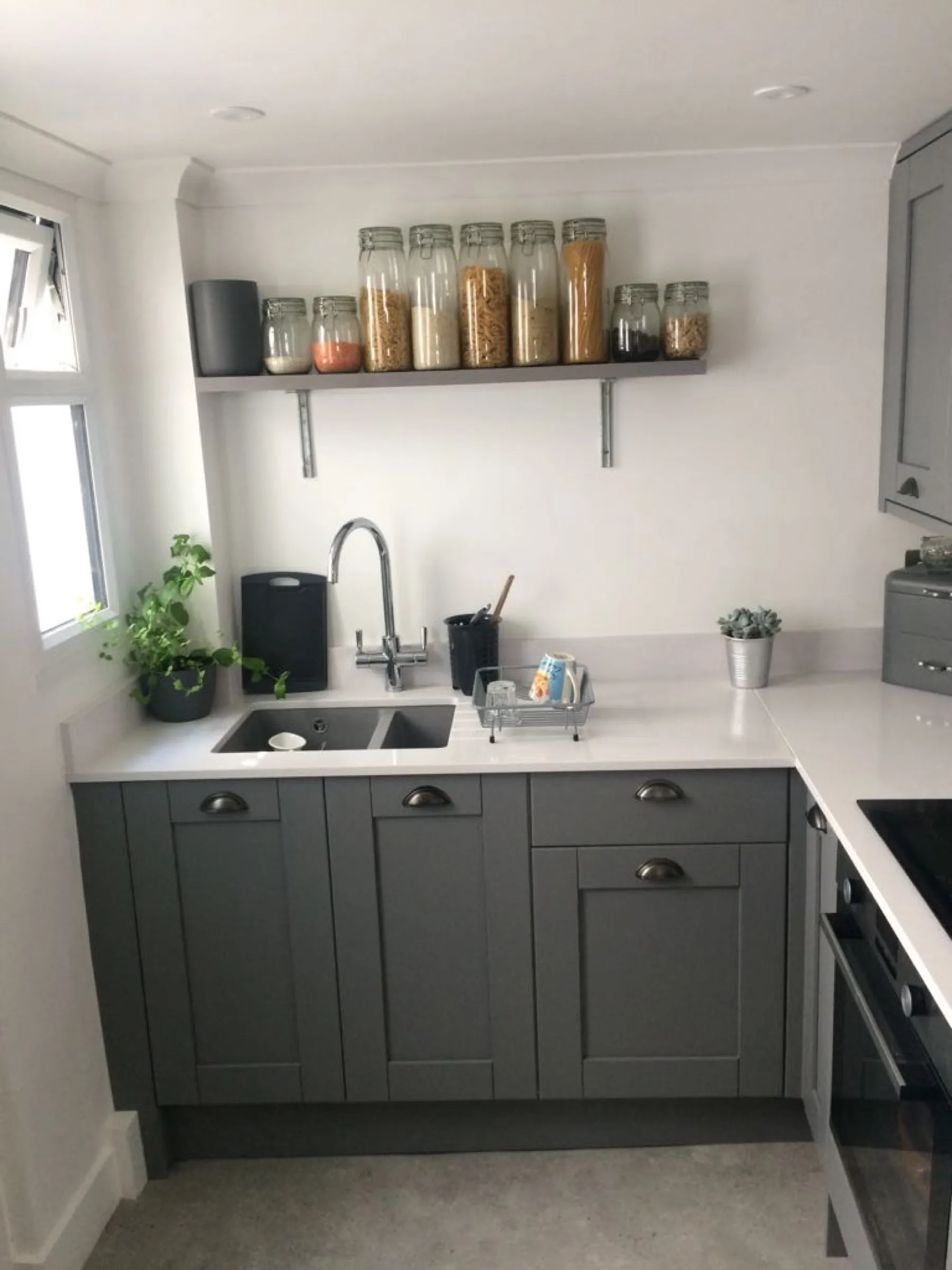 Compact grey Shaker kitchen with white worktops, chrome mixer tap and an open shelf of storage jars