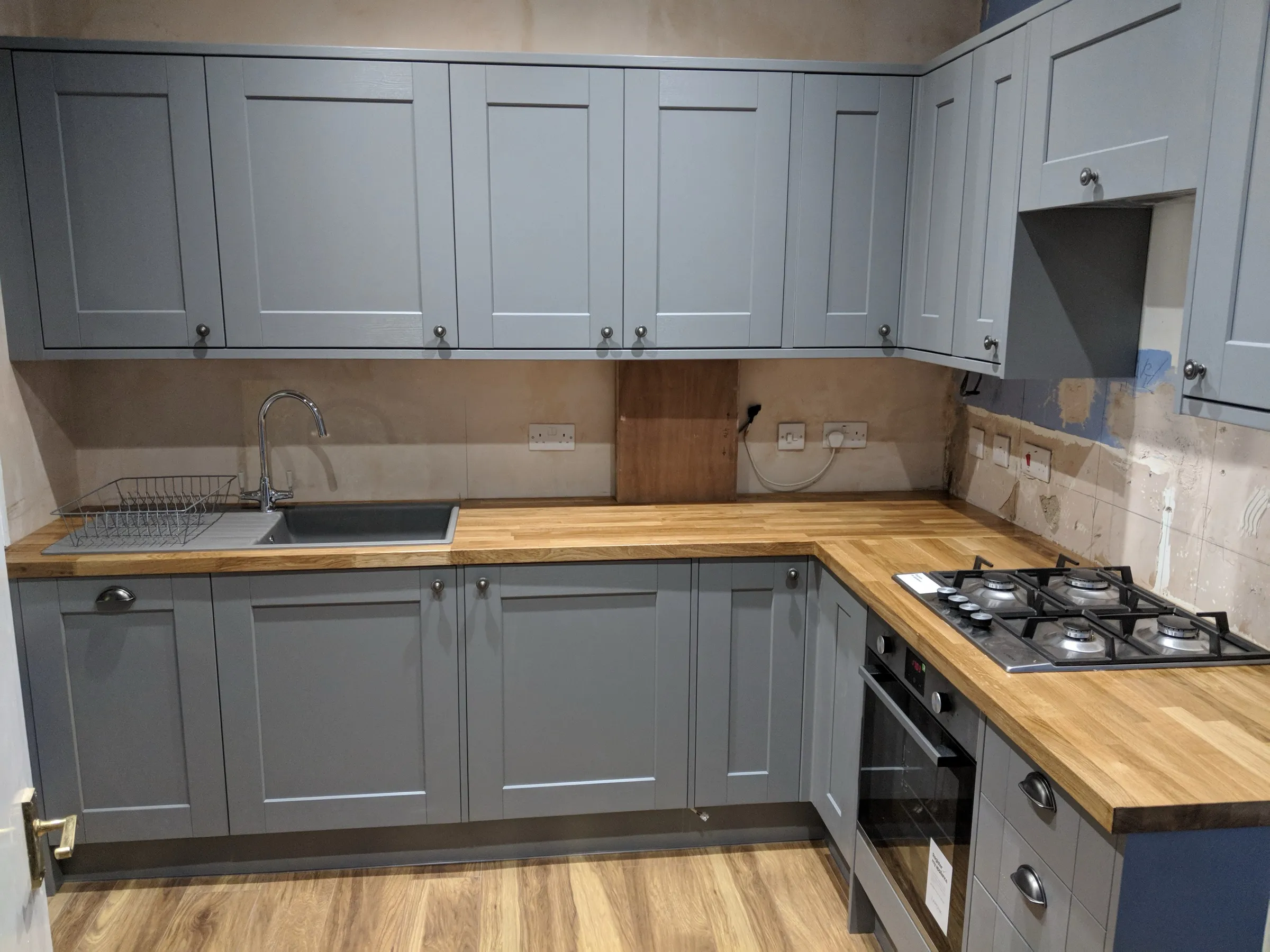 L-shaped grey Shaker kitchen with pewter handles, solid oak worktops, grey composite sink and five-burner stainless steel gas hob, photographed before decoration